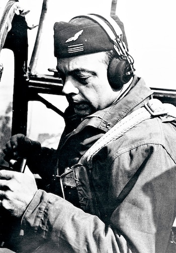Fotografía en blanco y negro de Antoine de Saint-Exupéry en la cabina de un avión, con uniforme, gorro de piloto y auriculares, manipulando controles