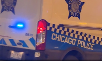 Parte trasera de un vehículo policial blanco con la inscripción Chicago Police, un escudo y luces azules encendidas