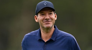 Un hombre de mediana edad con gorra oscura y polo azul marino mira de frente sonriendo ligeramente, con un fondo verde borroso