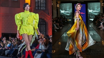 Dos modelos caminan por una pasarela: una viste un conjunto amarillo con calcetines rojos y la otra lleva un vestido largo multicolor.