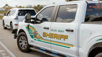 Primer plano de una camioneta policial blanca con el logotipo del sheriff del condado de Collier, luces de emergencia y una camioneta SUV blanca detrás