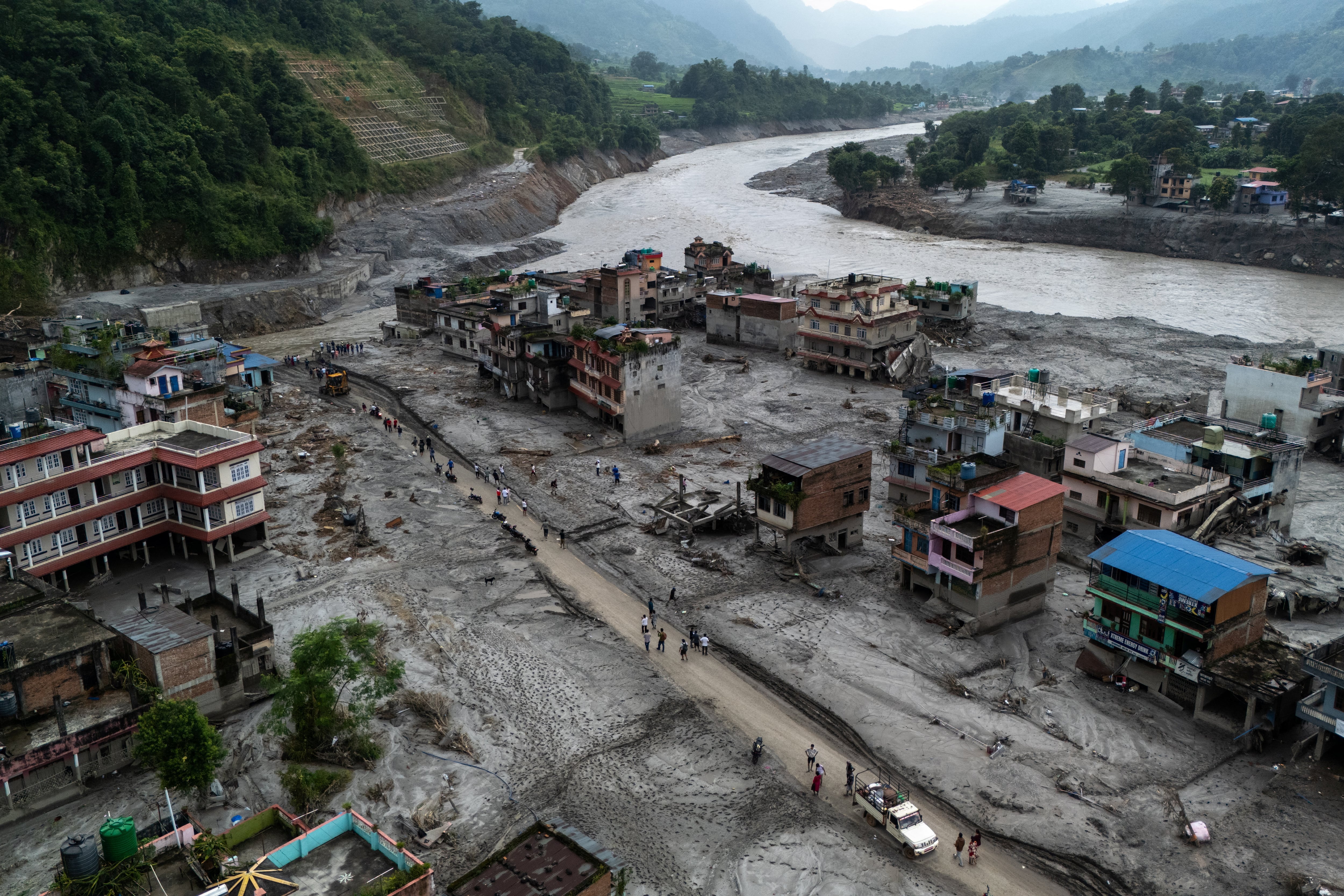 Vista desde un dron de personas caminando por una carretera y casas cubiertas de barro tras las mortales inundaciones repentinas y deslizamientos de tierra en Devighat, distrito de Nuwakot, Nepal, el 29 de agosto de 2026 (REUTERS/Athit Perawongmetha)