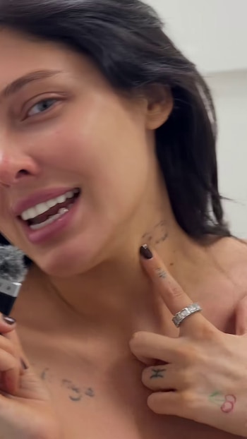 Plano medio corto de una mujer con cabello oscuro que señala un tatuaje en el lado izquierdo de su cuello