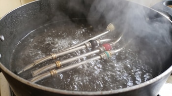 Tres bombillas de metal con detalles decorativos dentro de una olla llena de agua hirviendo con vapor.