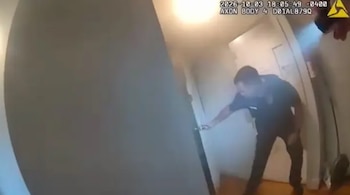 Toma de cámara corporal de un policía con uniforme oscuro que alcanza el picaporte de una puerta en el interior de una vivienda con humo