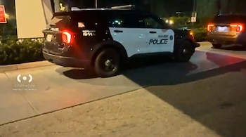 Un vehículo policial blanco y negro estacionado de noche en una vía con las luces traseras encendidas