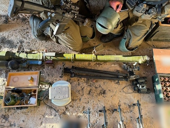 Vista superior de soldados con uniforme militar junto a un lanzacohetes, un trípode, binoculares, cajas de munición y otras armas en el suelo