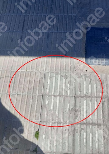 Primer plano de un trozo de acera gris con baldosas desgastadas y un pequeño hueco, rodeado por un círculo rojo, junto a una tapa de alcantarilla