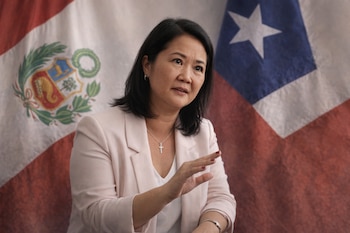 Mujer de cabello oscuro y blazer claro gesticula con la mano derecha. Detrás, se observan las banderas de Perú con su escudo y Chile con una estrella.