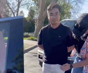 Un hombre con gafas y camiseta negra, identificado como Bryan Vejar, es sujetado por otra persona con gorra y camisa estampada. Fondo borroso con árboles
