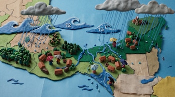 Mapa de plastilina y tela con casas, árboles, ríos, dos nubes de lluvia, ondas marinas numeradas 12 y 13, y figuras con paraguas.