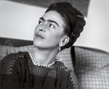 Retrato en blanco y negro de Frida Kahlo con cabello recogido, cejas pronunciadas, collar y pendientes, en una blusa bordada