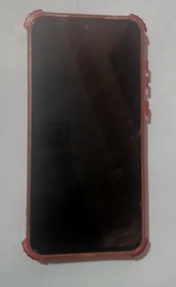 Teléfono inteligente con pantalla oscura y funda protectora de color rosado o salmón, colocado sobre una superficie clara y lisa