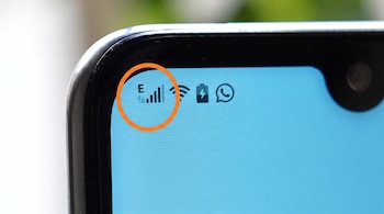 Parte superior de un teléfono inteligente con pantalla azul claro. Se ven iconos de letra E, barras de señal móvil, Wi-Fi, batería cargando y WhatsApp.
