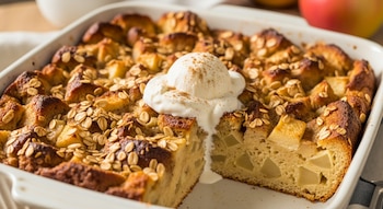 Budín de pan con trozos de manzana y avena en un molde blanco, con un trozo cortado y una bola de helado con canela encima.