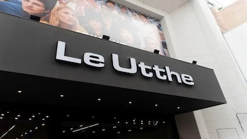 Primer plano del letrero de la tienda Le Utthe en letras blancas sobre una superficie negra. Sobre el letrero, un gran anuncio con modelos