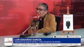 Hombre en mesa con micrófono rojo de Radio Nacional, vaso de agua y libro en atril que muestra un traje negro