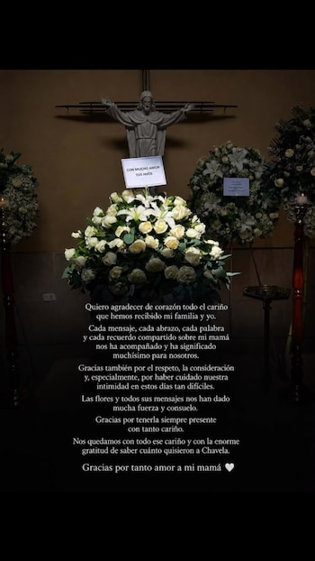 Arreglo floral grande de rosas y lirios blancos con una tarjeta que lee 'Con mucho amor tus hijos' frente a una estatua de Jesús y velas