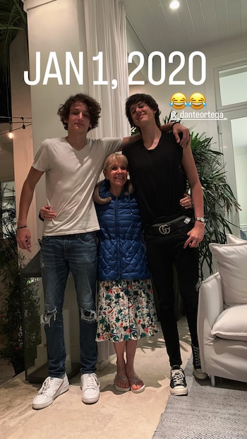 Evangelina Salazar, mujer rubia sonriente de chaqueta azul, flanqueada por dos hombres jóvenes, uno con camiseta blanca y otro con top negro, en un interior