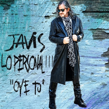 Hombre con cabello gris, barba, gafas de sol, gabardina larga de cuero negra, bufanda estampada, pantalones negros y botas negras, de pie ante una pared azul craquelada con texto