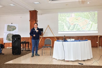 Personas sentadas en varias mesas de un salón atienden a una exposición proyectada en una pantalla al frente