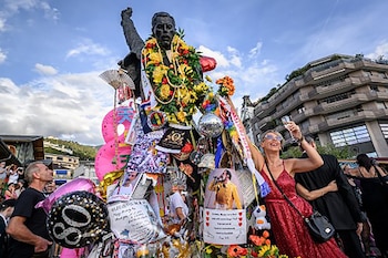 Estatua de bronce de Freddie Mercury cubierta de flores, carteles y un globo con el número 80, rodeada por admiradores