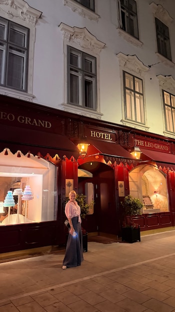 Yanina Latorre posa frente a la fachada iluminada de un hotel con toldos rojos y ventanales con decoraciones de pasteles en Viena, Austria