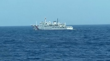 Un gran barco blanco de la Guardia Costera de China, con distintivos rojos y azules, surca aguas oceánicas agitadas bajo un cielo claro