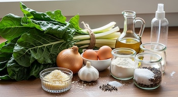 Una vista de ingredientes frescos incluyendo acelga, cebolla, ajo, dos huevos en un cuenco, harina, queso rallado, sal, pimienta y aceite en recipientes de vidrio, sobre una mesa de madera.
