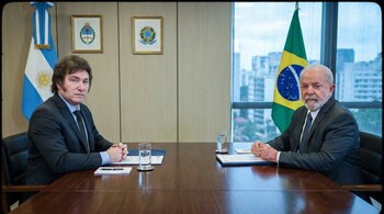 Javier Milei y Luiz Inácio Lula da Silva sentados en una mesa frente a frente. Fondo con banderas de Argentina y Brasil, vasos de agua y papeles.