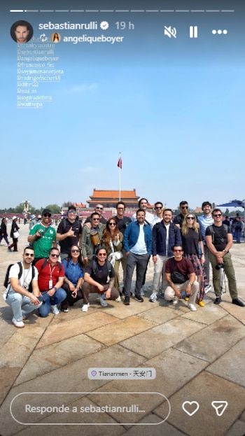 Grupo de veinte personas posando al aire libre frente a la Puerta de Tiananmén en Pekín bajo un cielo azul claro, con una bandera roja ondeando