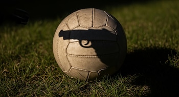 Balón de fútbol clásico sobre césped con la sombra de una pistola en su superficie.