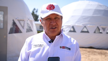 Pedro Morales viste una gorra con el escudo de Perú y una camisa con el logo de Pronied delante de dos domos modulares blancos