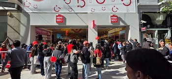 Multitud de personas haciendo fila en la entrada del primer local de Miniso, con globos rojos y el logotipo de la marca claramente visible en la fachada blanca