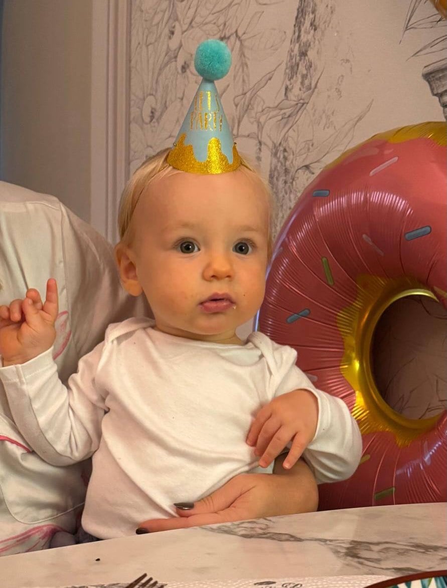 Vicente, hijo de Muni, luciendo un gorro de fiesta azul claro y dorado y un globo en forma de donut durante la celebración de su primer cumpleaños
