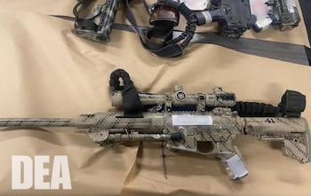 Dos armas de fuego camufladas, una de ellas un rifle con mira telescópica, sobre una superficie marrón. Logotipo DEA en la esquina inferior izquierda