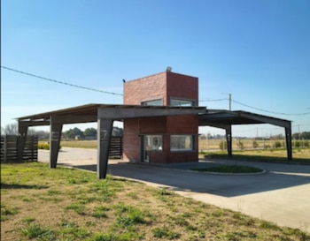 Entrada principal a un country club con garita de seguridad de ladrillo rojo, cubierta metálica y césped, bajo un cielo azul despejado