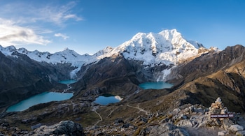 Paisaje andino con el Nevado Tocllaraju nevado, lagunas turquesas y valles rocosos. Un cairn con un letrero de 'Nevado Tocllaraju - Perú' en primer plano.