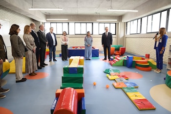 Un grupo de adultos vestidos de manera formal observa una sala infantil con colchonetas de colores, bloques de espuma y una alberca de pelotas
