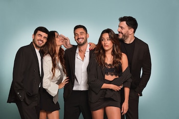 Cinco personas con vestimenta formal en tonos oscuros posan y sonríen delante de un fondo azul claro