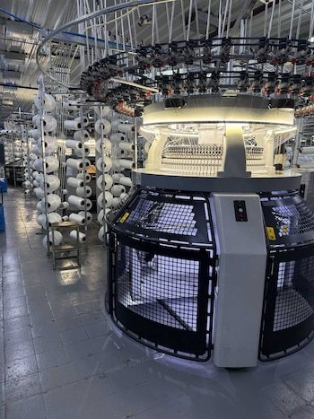 Una máquina industrial circular iluminada frente a varias estructuras con bobinas de hilo blanco