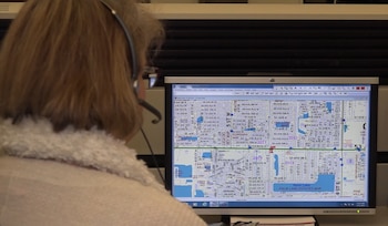 Persona con audífonos observa una pantalla de computadora que muestra un mapa digital con calles y nombres de áreas. Se visualizan textos y números en la pantalla