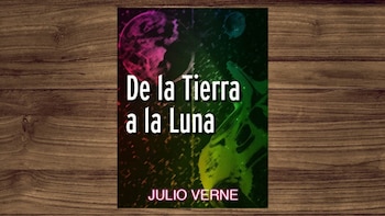 Un póster o portada de libro 'De la Tierra a la Luna' de Julio Verne. Presenta un diseño gráfico abstracto con planetas en tonos neón sobre un fondo oscuro, sobre madera