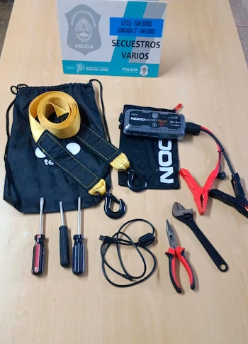 Destornilladores, pinza, llave inglesa, correa de remolque, arrancador de batería y cables junto a una caja de secuestros policial