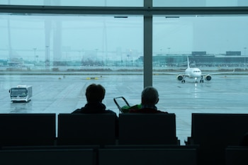 Dos personas esperan sentadas frente a un avión aparcado en la pista del aeropuerto de El Prat. (David Zorrakino/Europa Press)