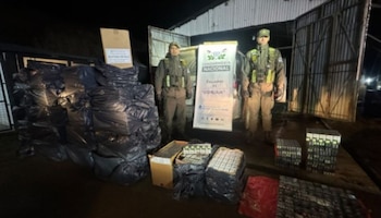 Dois policiais uniformizados estavam ao lado de uma pilha de canecas pretas e pacotes de cigarros, com inscrições da Guarda Nacional.