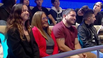 Vista lateral de tres personas sentadas en una audiencia: una mujer joven sonriente, una mujer mayor con gafas sonriente y un hombre barbudo sonriente