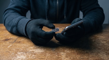 Manos con guantes negros sostienen una tarjeta SIM y un teléfono móvil sobre una mesa de madera.