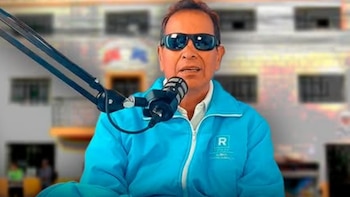 Un hombre con gafas de sol oscuras y casaca azul habla frente a un micrófono de estudio sobre un fondo urbano desenfocado