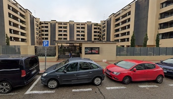 Vehículos estacionados en calle con edificios residenciales de múltiples plantas. Se observan garita de acceso, reja y una señal de aparcamiento